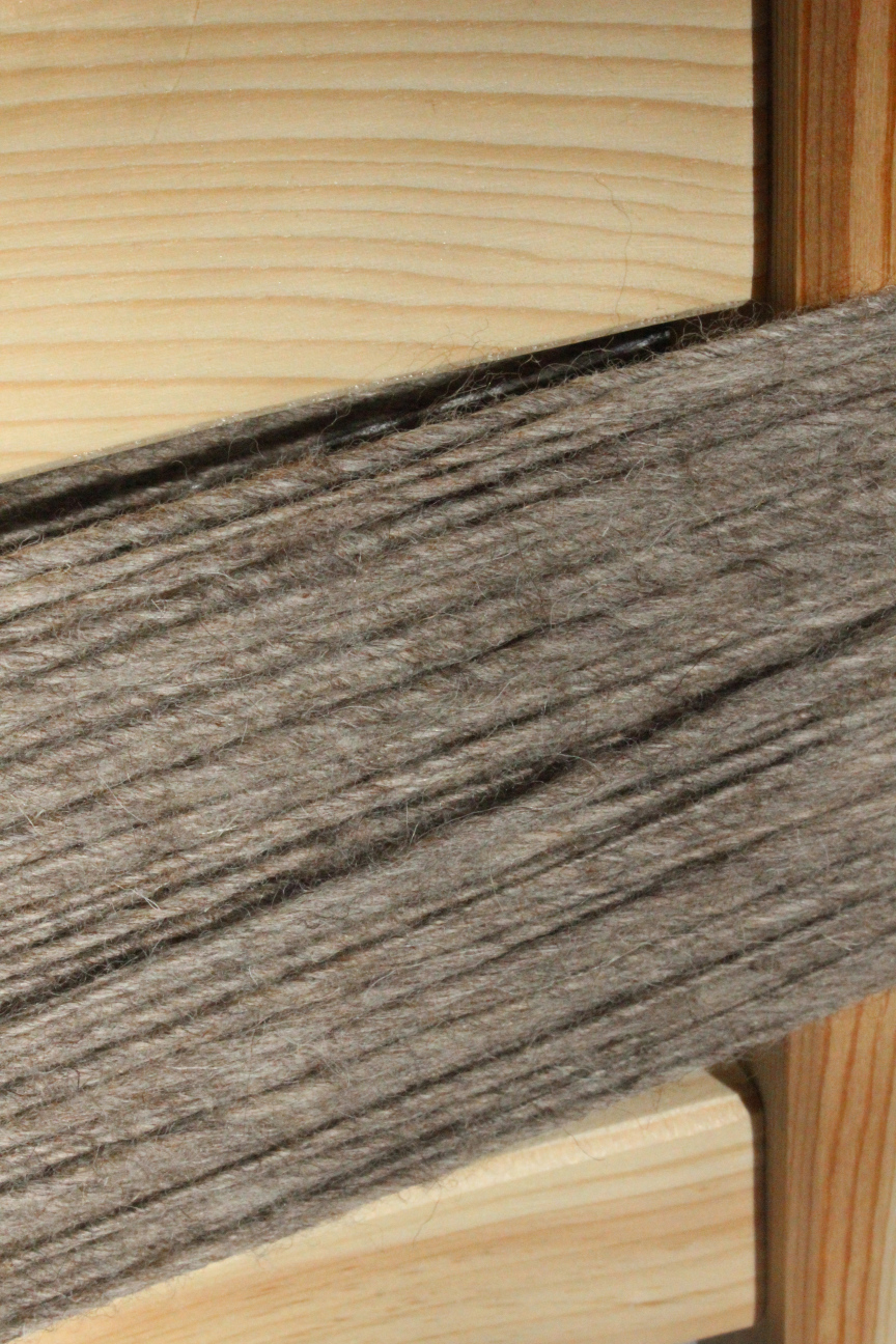 frisch versponnene Wollfasern in dunklen Sandfarben um die Lehne eines Kieferstuhls gewickelt   