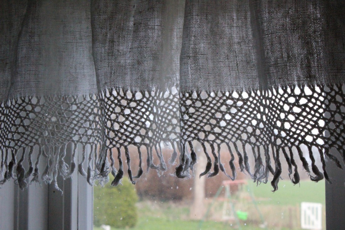 Ausschnitt einer weißen Stoffgardine mit Fransen in der Dämmerung