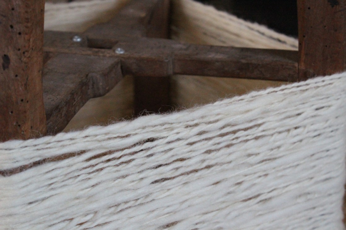 Nahaufnahme eines Strangs verzwirnter Eiderwolle, die auf den Beinen eines umgedrehten Holzhockers so rundherum aufgespannt wurde.
