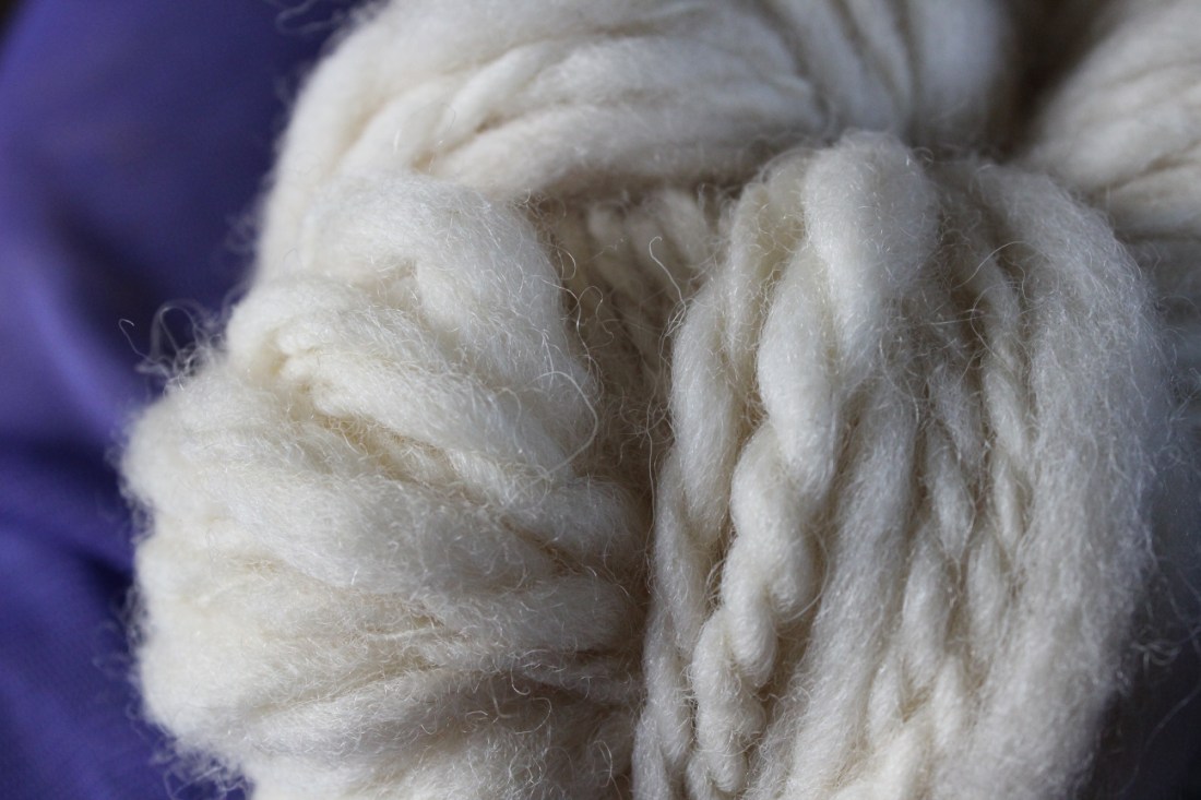 Fertiges Eiderwollgarn als Knäuel in Nahaufnahme, liegt auf einem Hintergrund aus lila Tüll.
