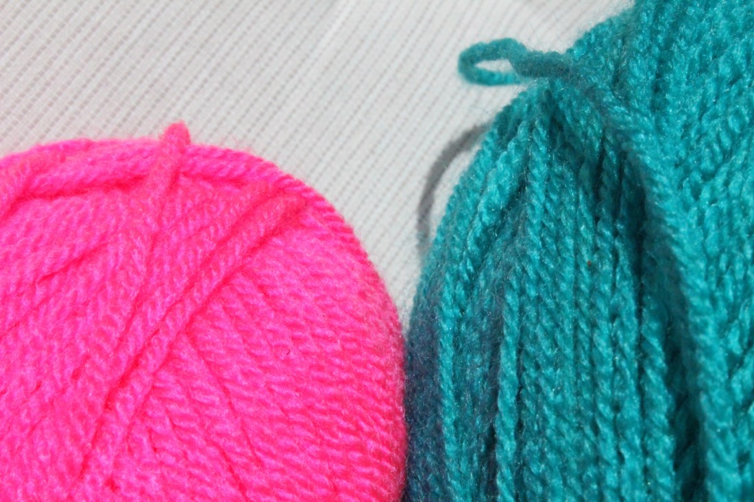 Kleines Knäuel pinkes Garn, großes Garn dunkeltürkises Garn, Nahaufnahme, nur ein ausschnitt beider Knäuel