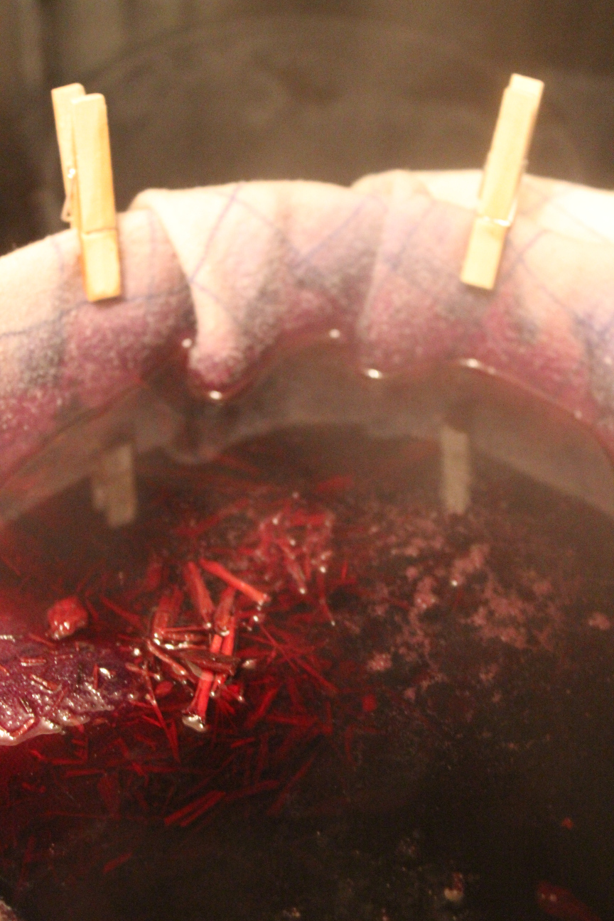 Färbebad, Blauholz in rotem Sud in einem Tuch, das mit Mini-Wäscheklammern am topf befestigt ist.