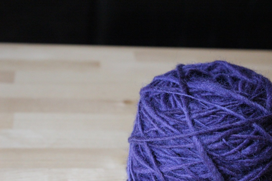 Knäuel dunkellila Garn, zur Kugel aufgewickelt.