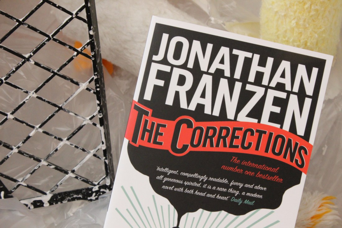 Das Buch "The Corrections" von Jonathan Franazen in einer Malereikiste mit Abrollgitter und Farbrollen im Hintergrund.