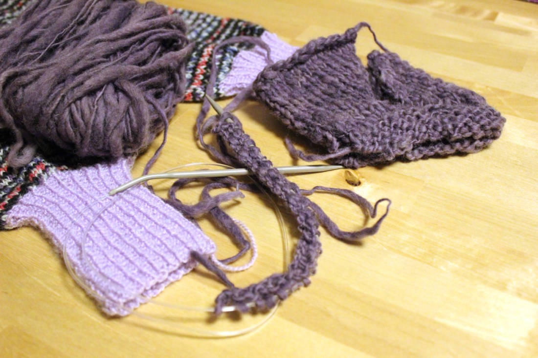 Strickfilzschuhe in the making, einer fertiggestrickt, aber noch nicht vernährt, ein anderer ganz am Anfang auf der Nadel.