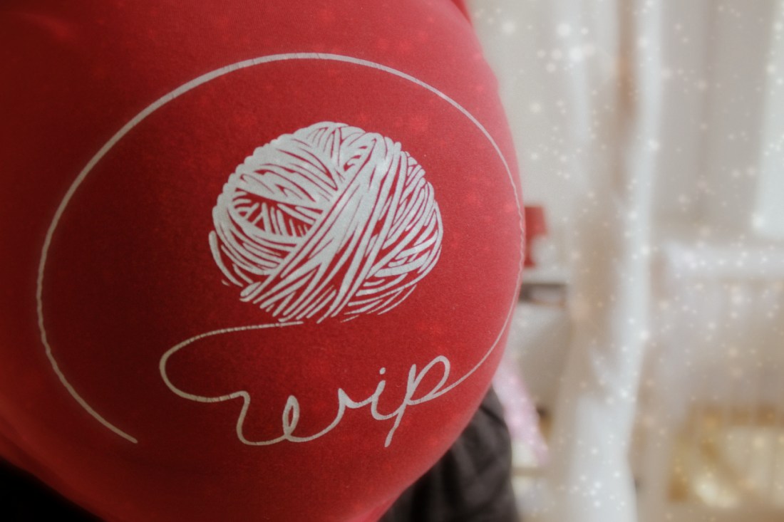 Bauchfoto, auf dem T-Shirt steht in kugelrunder Bauchhöhe "wip", die Buchstaben schlängeln sich aus einem gezeichneten Wollknäuel.