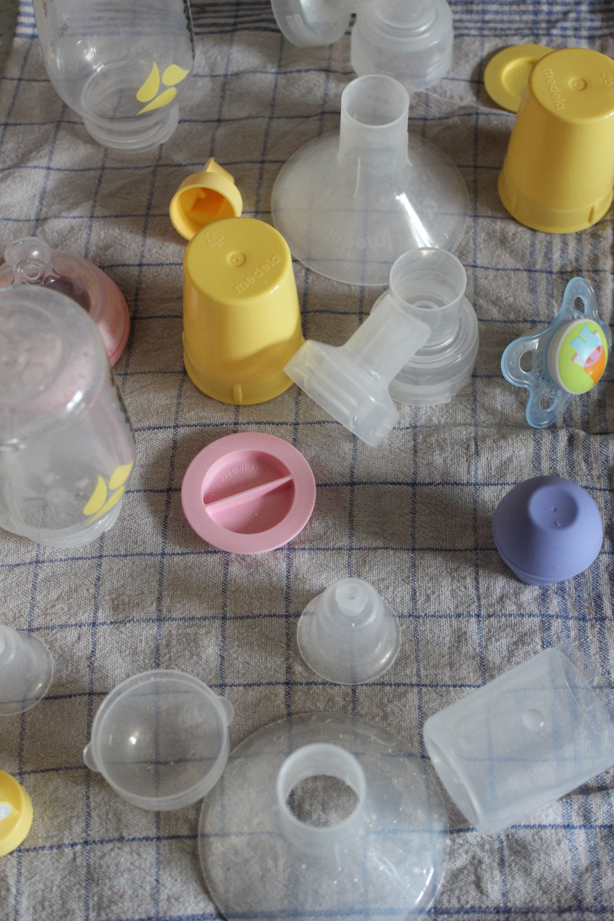 Fläschchenaccesoires, Aufsätze für Milchpumpen, Stillhütchen, Schnuller und Vakuumgrößermachdingsis für Nippel, ausgebreitet auf einem Geschirrhandtuch mit blauen Karos, nach dem Waschen und Sterilisieren.