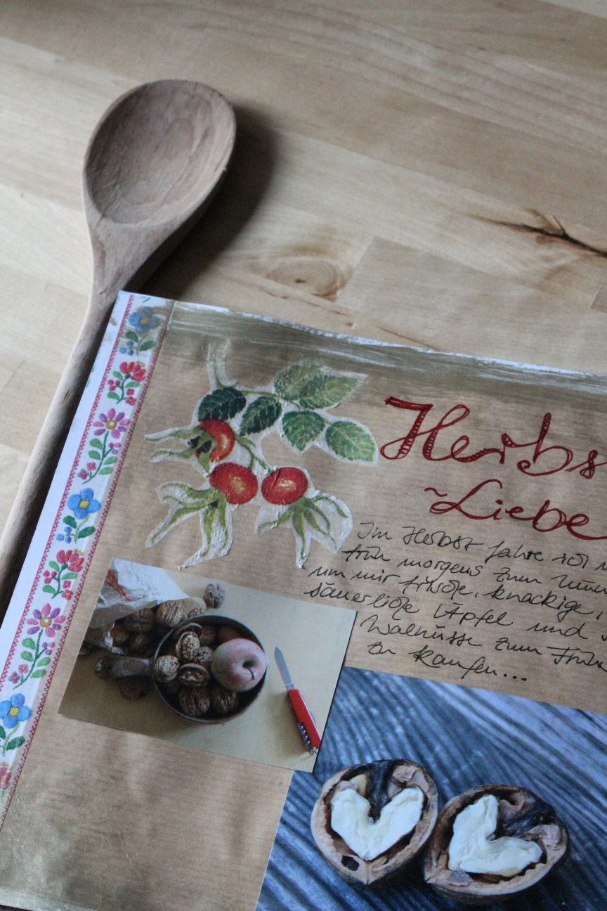 Eine Seite mit Fotos von Äpfeln und Walnüssen mit herzförmigem Nusskern, daneben liegt ein Kochlöffel aus Holz.