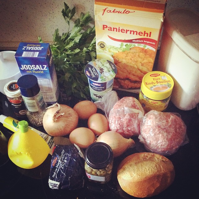 Paniermeh, Hackfleisch, Eier, Mehrl, Rinderbrühe, Brötchen, Kapern, Butter, Zitronensaft, Zwiebeln, Sahne, Salz, Petersilie, Piment, Sardellenpaste und mehr, auf dem Elektroherd dekorativ zusammengestellt.