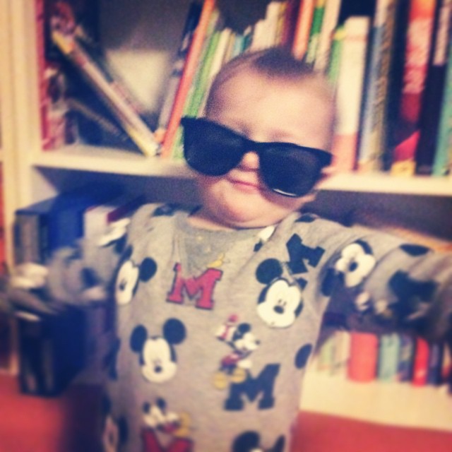 Kind in Sonnenbrille, die etwas von der Nase rutscht, es breitet seine Arme aus.