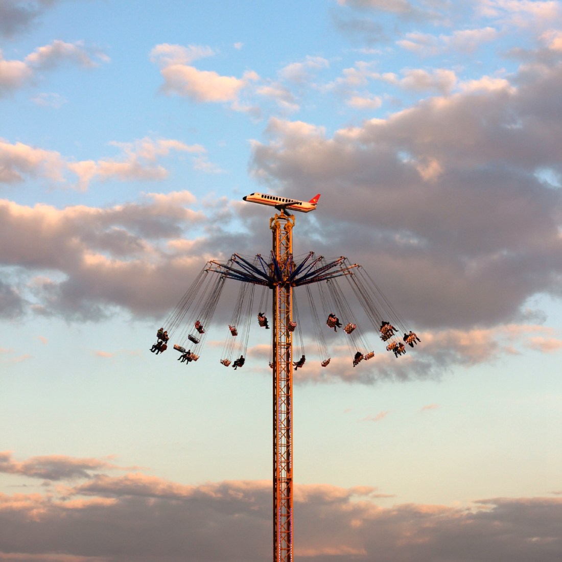 Kettenkarussel hoch in der Luft, an einem Turm. an dessen Spitze ein Flugzeug befestigt ist. 